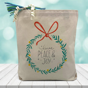 Love, Peace & Joy inside of a wreath printed on a canvas tote bag sitting on a wood table