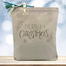 merry christmas printed on a canvas tote bag sitting on a wood table with a snowflake background