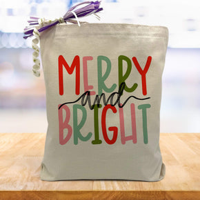merry & bright in colorful letters printed on a canvas tote bag sitting on a wood table