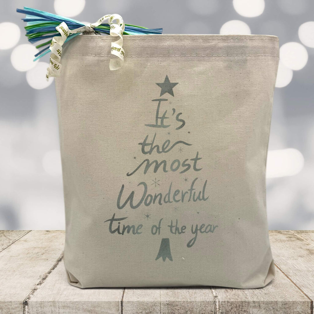 Its the most wonderful time of the year in silver printed on a canvas tote bag sitting on a wood table