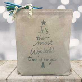Its the most wonderful time of the year in silver printed on a canvas tote bag sitting on a wood table