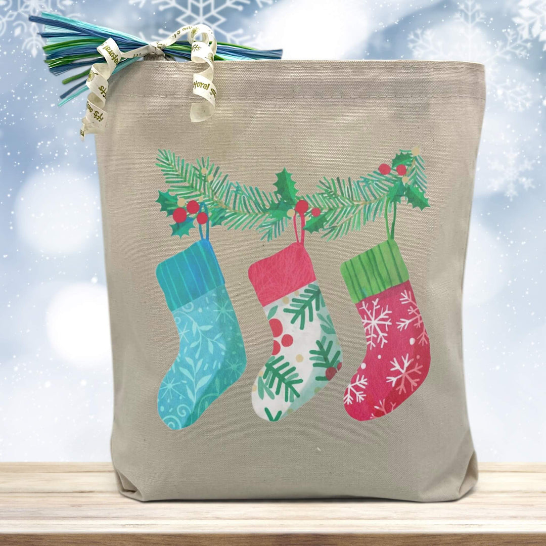 3 stockings hanging printed on a canvas tote bag sitting on a wood table with a blurred blue background