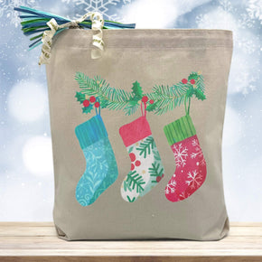 3 stockings hanging printed on a canvas tote bag sitting on a wood table with a blurred blue background