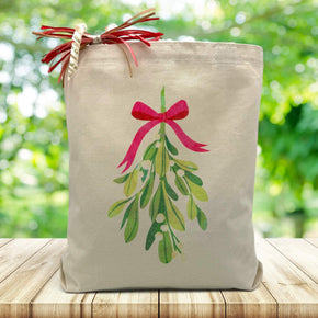 holiday mistletoe printed on a canvas tote bag sitting on a wood table with a blurred green background