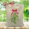 holiday mistletoe printed on a canvas tote bag sitting on a wood table with a blurred green background