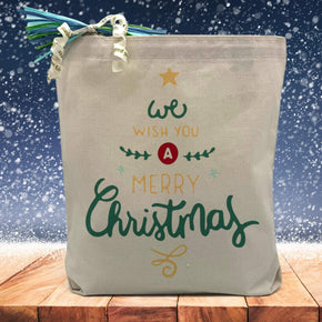 we wich you a merry christmas printed on a canvas tote bag sitting on a table with a snowflake background