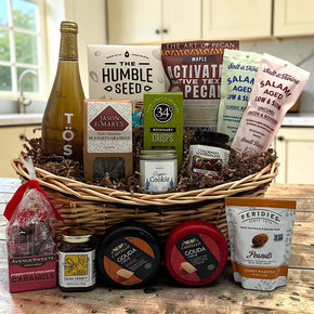 Wicker basket with sparkling juice, crackers, pecans, salamis, caramels, cheeses, honey, peanuts and a candle