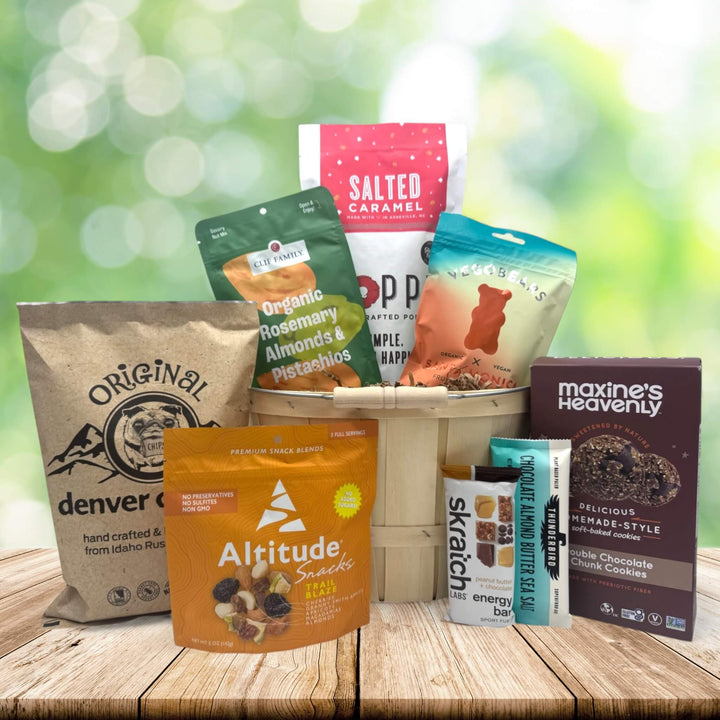 Assorted healthy snacks including trail mix, protein bars, and cookies in a wooden gift basket on a wooden table