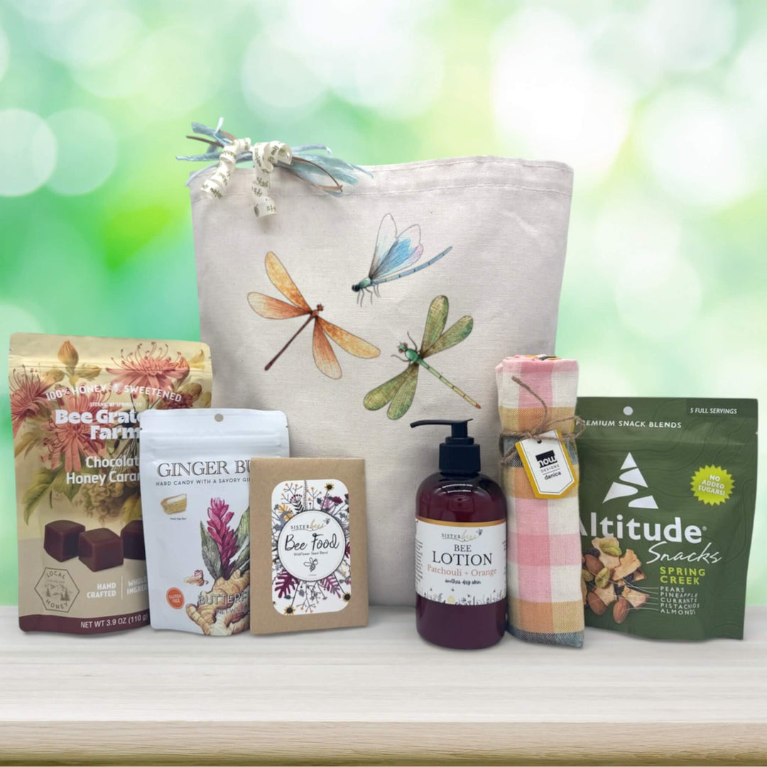 three dragonflys of blue, orange and green flying around on a tote bage with snacks sitting on wooden table