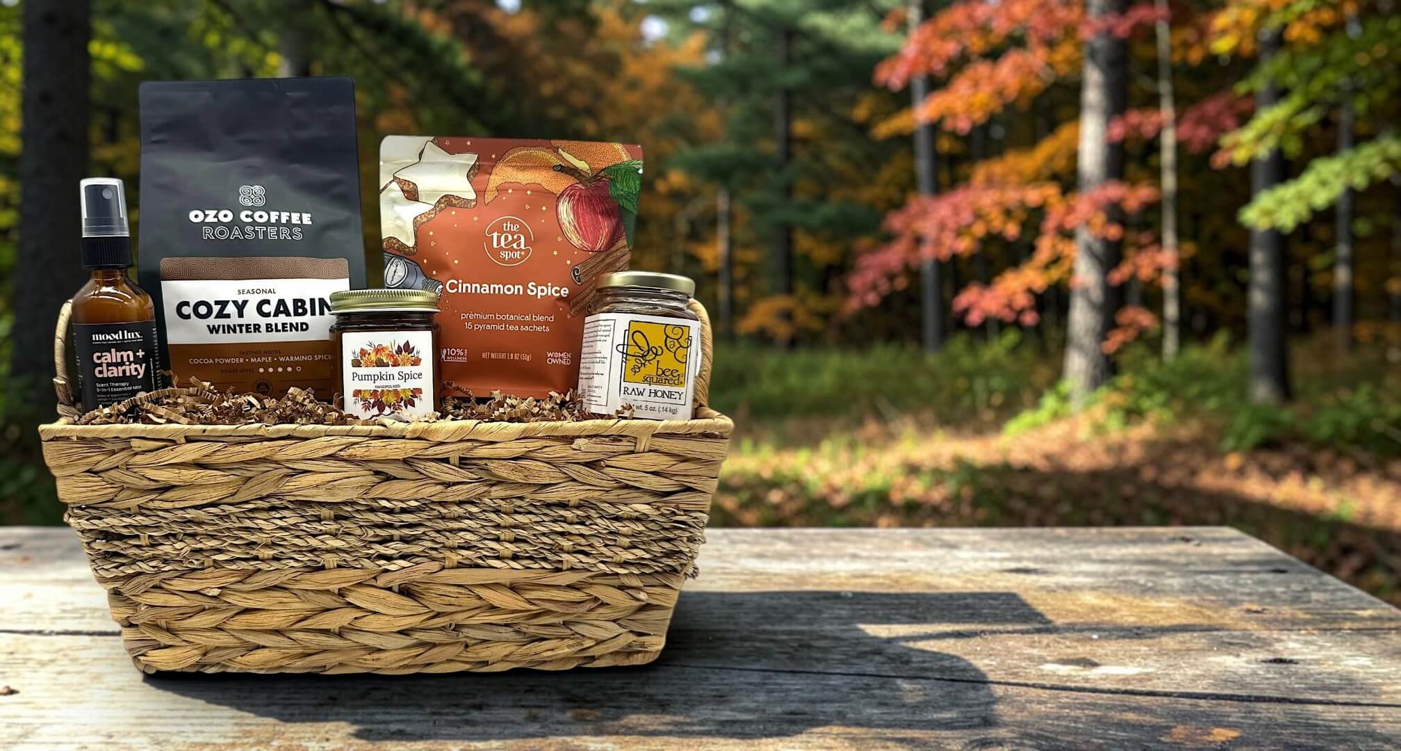 fall themed gift basket with coffee, tea, candle, honey and a calming spritz with a fall background