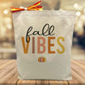 Fall vibes printed on a canvas tote bag sitting on a table with a blurred background