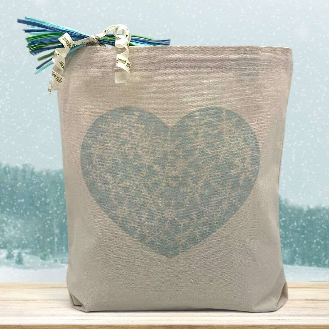 snowflake blue heart printed on a canvas tote bag sitting on a table with a snowflake background