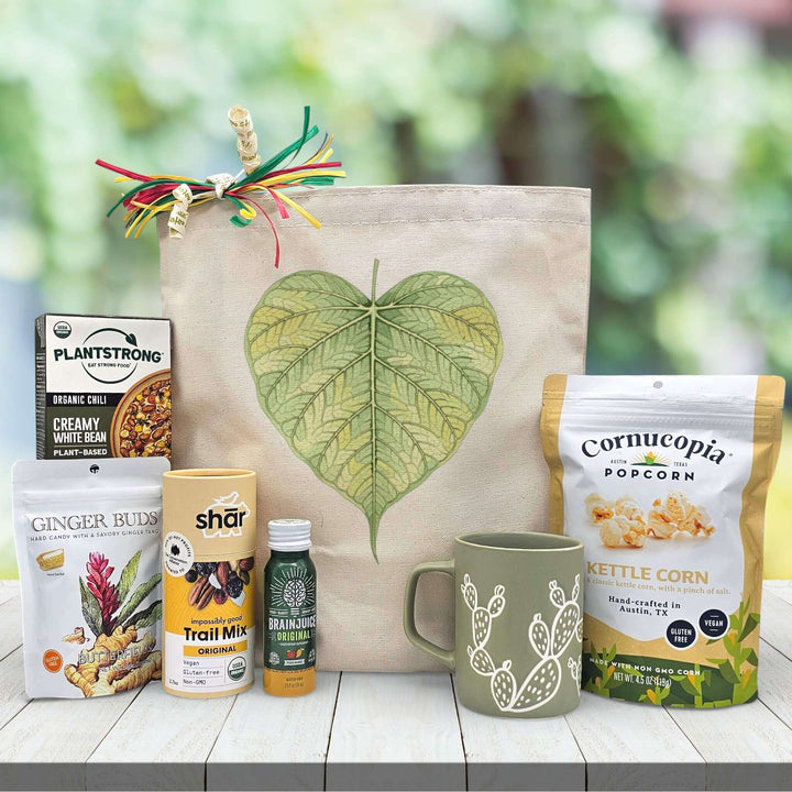 Eco-friendly gift set with canvas tote bag, cactus mug, kettle corn, trail mix, and organic snacks on a white table
