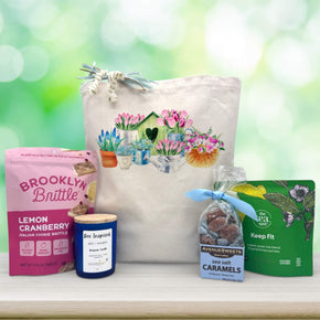 flowers surrounding a bird house with a watering can printed on a back with snacks and a candle sitting on a table