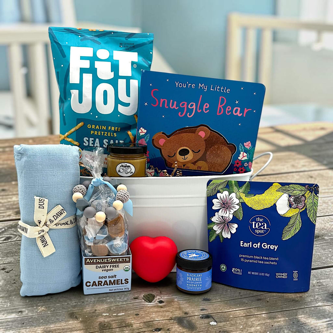 White tin tub with pretzels, a bear book, a swaddle, a teething ring, caramels, heart squeeze, honey and tea