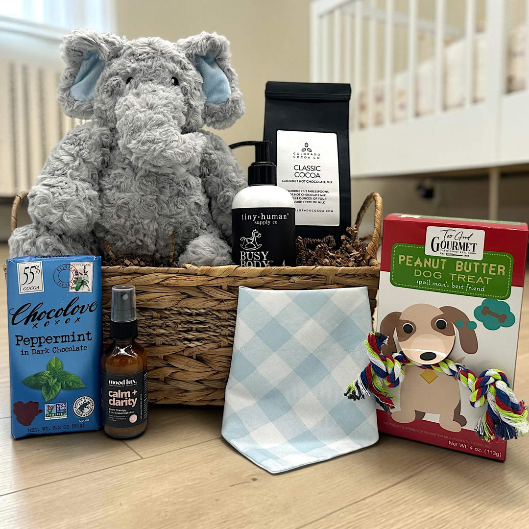 wicker basket with a stuffed elephant, baby shampoo, cocoa, chocolate bar, calming spritz, a dog bandana, and dog treat
