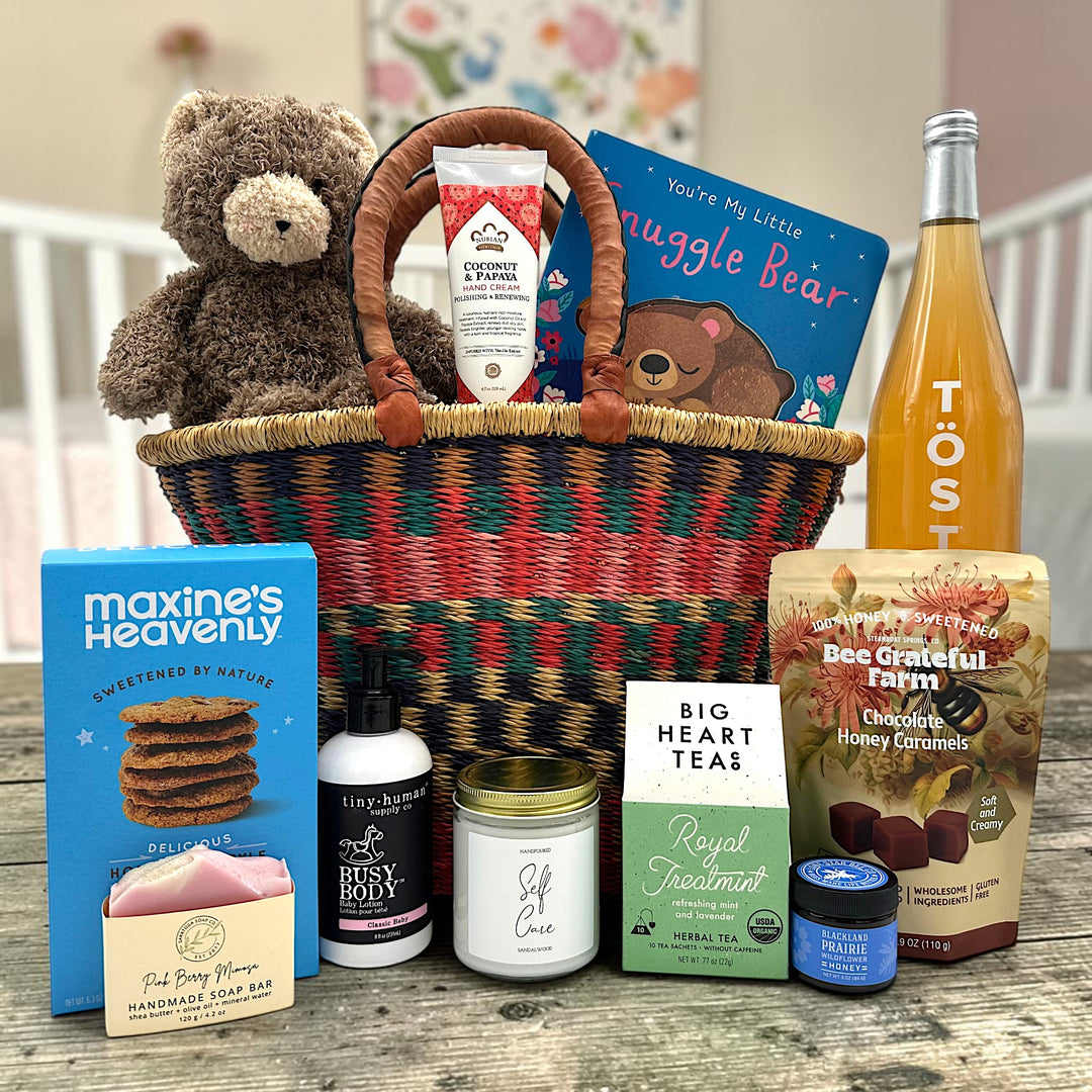 handwoven basket with a bear, lotion, a childrens book, cookies, soap, candle, tea, honey, caramels and sparkling juice