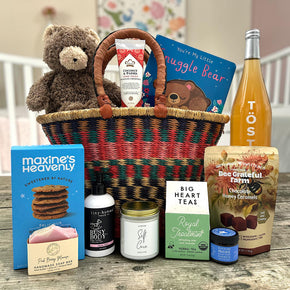 handwoven basket with a bear, lotion, a childrens book, cookies, soap, candle, tea, honey, caramels and sparkling juice