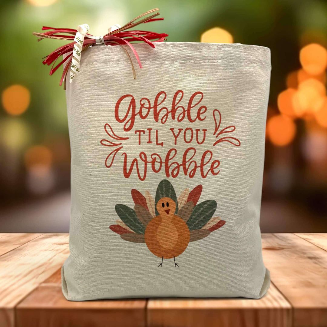 Gobble til you wobble with a turkey printed on a canvas tote bag sitting on a table with a blurred background