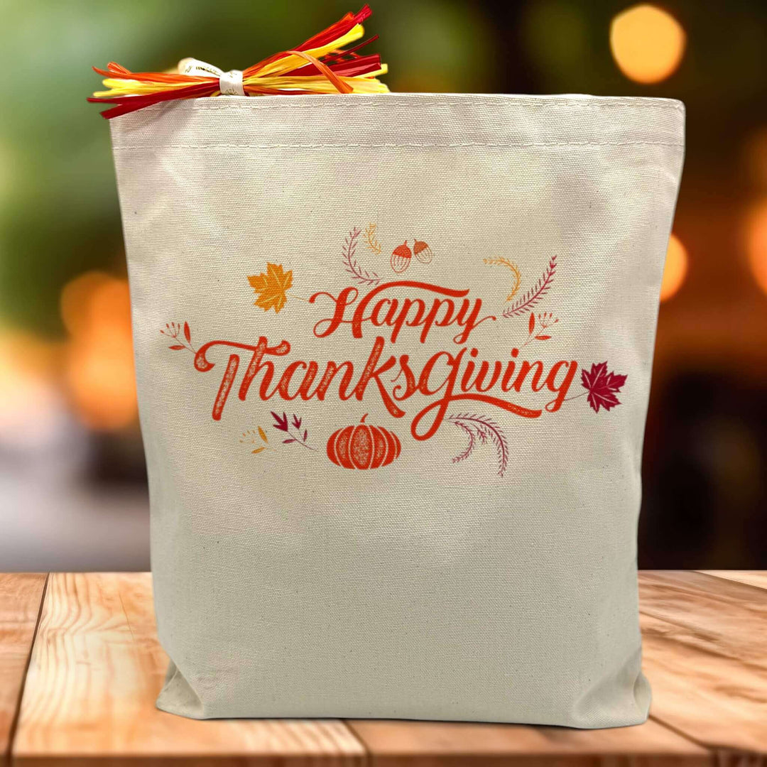 happy thanksgiving with leaves and pumpkin printed on a canvas tote bag sitting on a table
