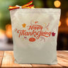 happy thanksgiving with leaves and pumpkin printed on a canvas tote bag sitting on a table