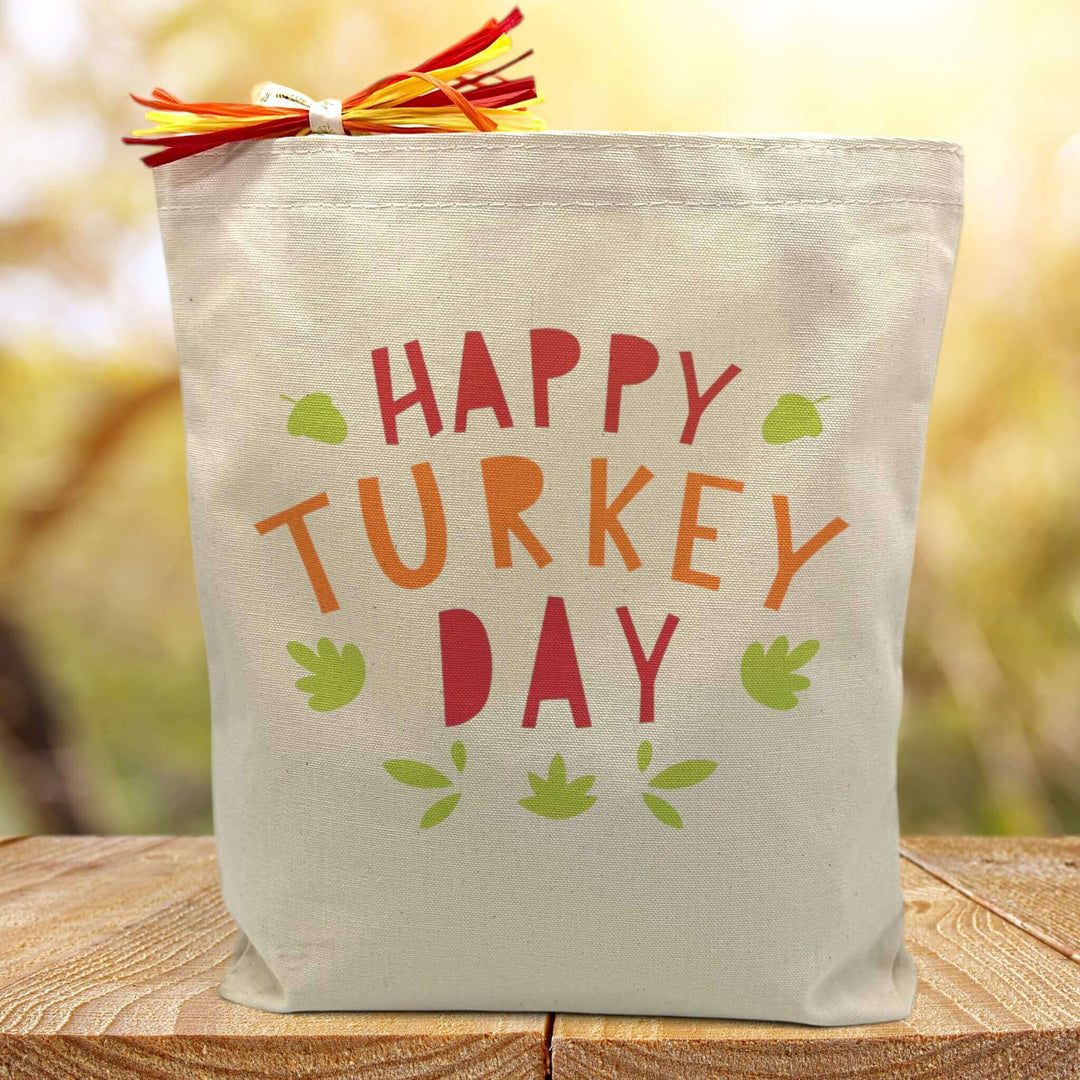 happy turkey day in colorful letters printed on a canvas tote bag sitting on a table with a blurred background