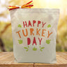 happy turkey day in colorful letters printed on a canvas tote bag sitting on a table with a blurred background