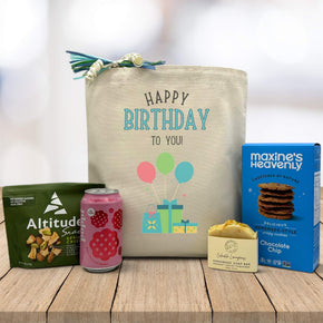 happy birthday to you written on tote bag sittign on table with trailmix, poppi soda, lemon soap, and chocolate chip cookies