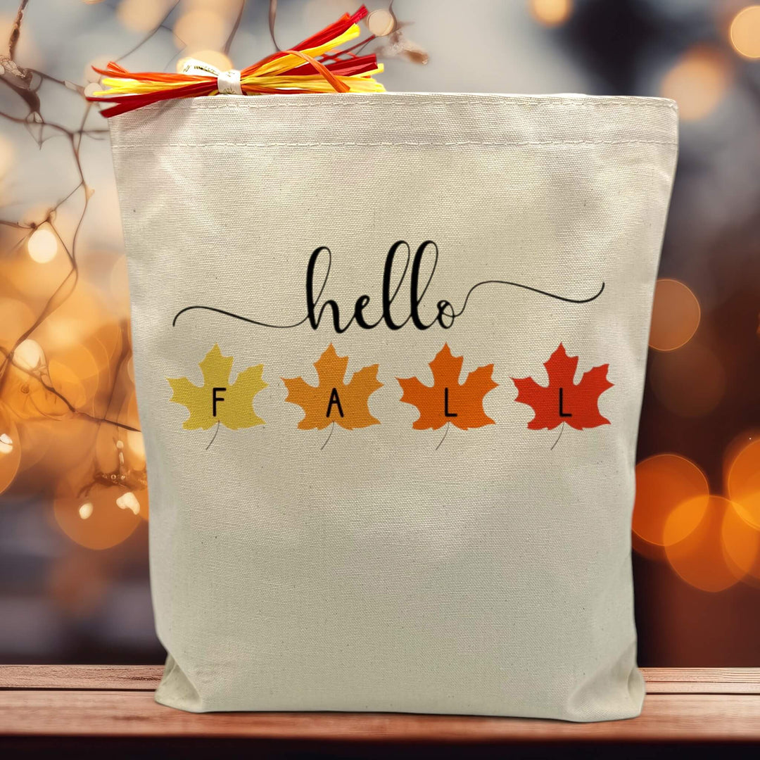 hello script with the word fall in leaves printed on a canvas tote bag sitting on a table