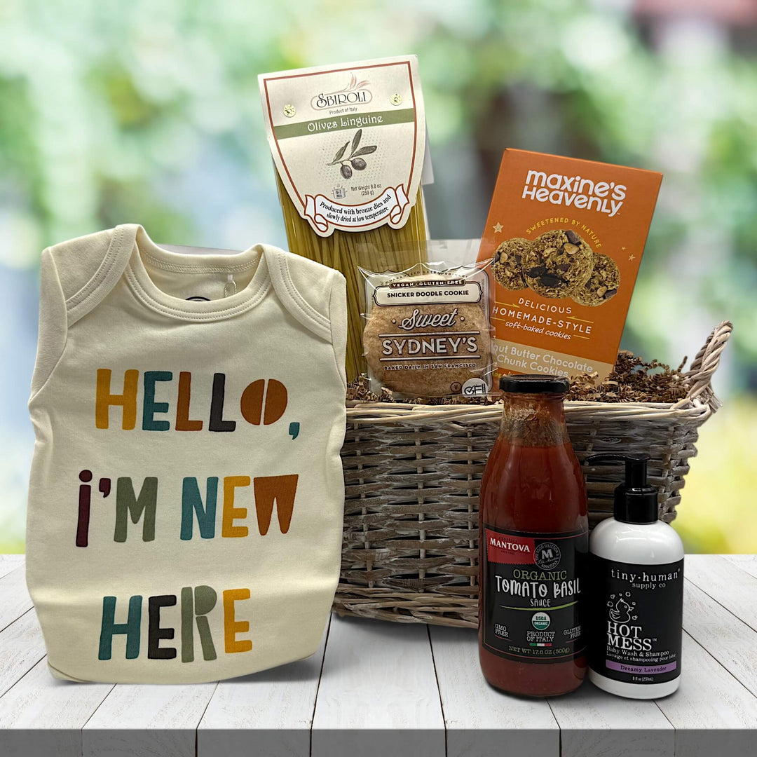 hello im new here onsie, pasta, pasta sauce, cookies and baby shampoo with a wicker basket sitting on a table