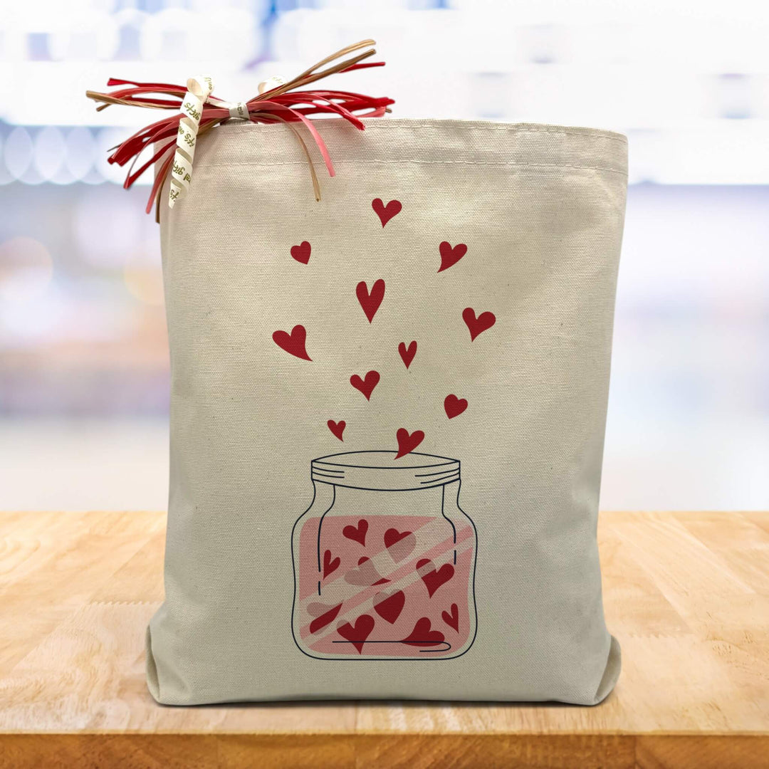 jar with red hearts printed on a canvas tote bag sittin gon a wood table with a blurred white background