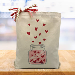 jar with red hearts printed on a canvas tote bag sittin gon a wood table with a blurred white background