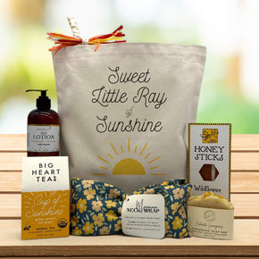 "Sweet little ray of sunshine" printed on tote bag with lotion, tea, neck wrap, soap, and honey sitting on table