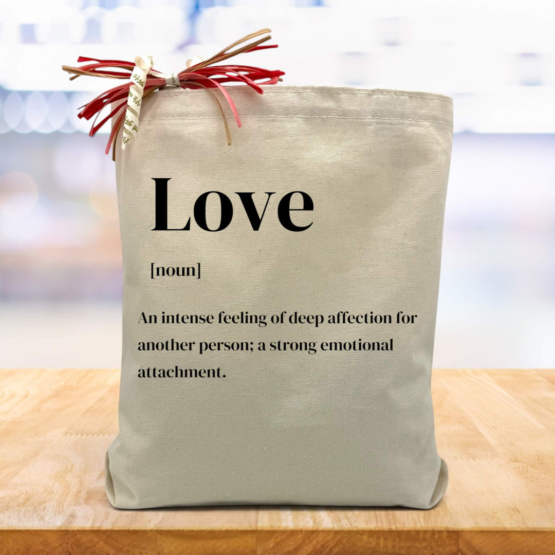 definition of love printed on a canvas tote bag sitting on a wood table with a blurred white background