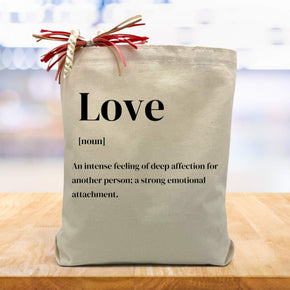definition of love printed on a canvas tote bag sitting on a wood table with a blurred white background