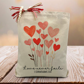 corinthians 13:8 love never fails printed on a canvas tote bag with hearts sitting on a rustic table
