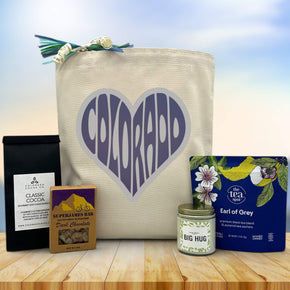 Colorado written in heart on tote bag sitting on table with cocoa, superjames bar, candle and tea