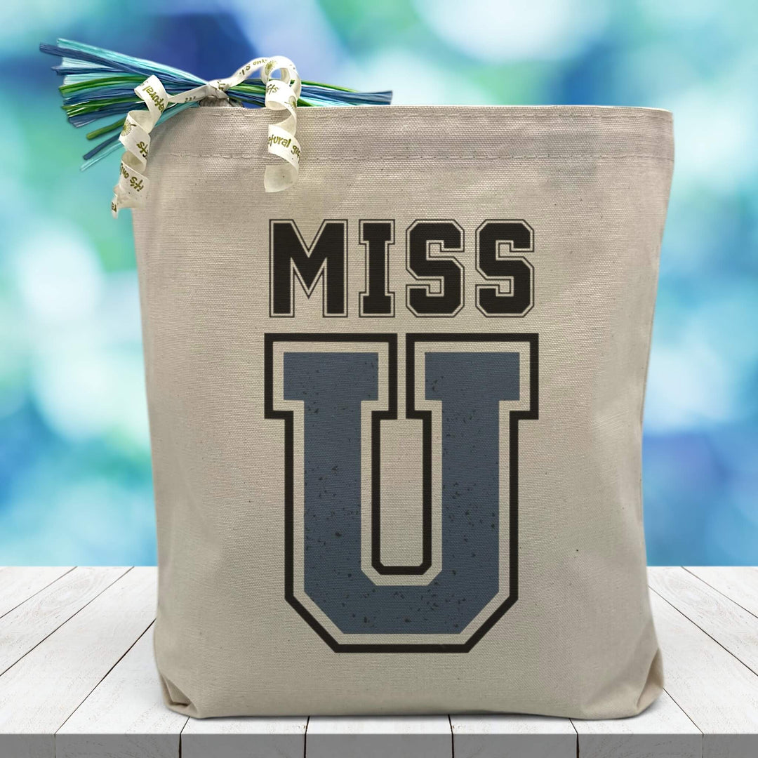 Miss U printed on canvas tote bag sitting on table with blue blurred background