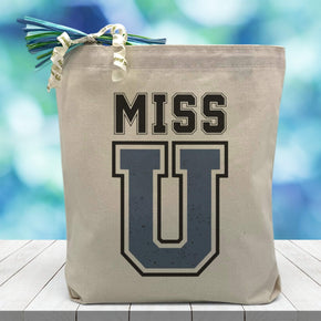 Miss U printed on canvas tote bag sitting on table with blue blurred background