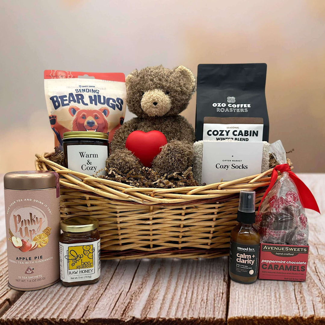 Wicker basket with taffy, a bear, coffee, socks, a heart squeeze, a large candle, tea, honey, and caramels