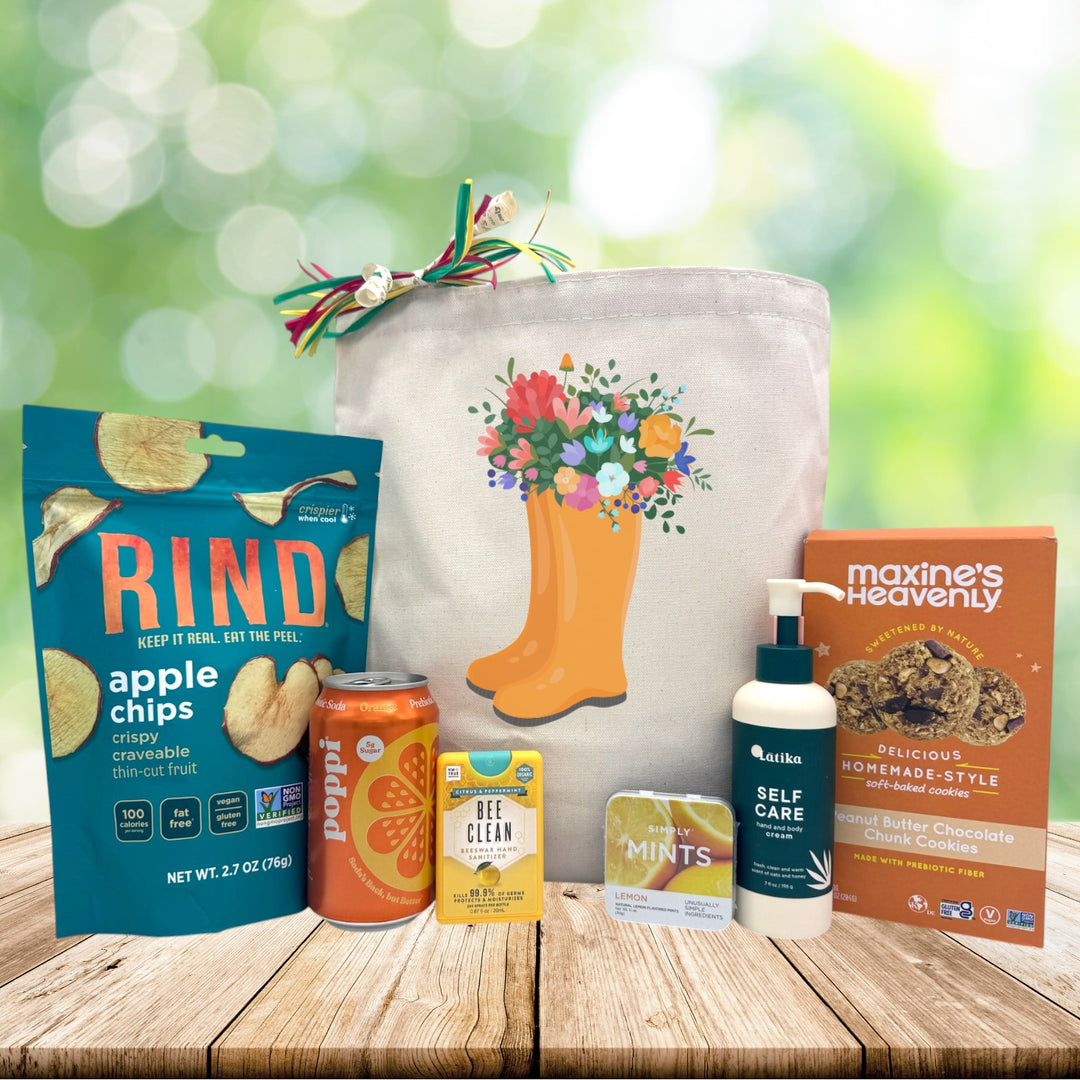 Orange rainboots with flowers coming out the top with snacks and self care lotion sitting on a wooden table