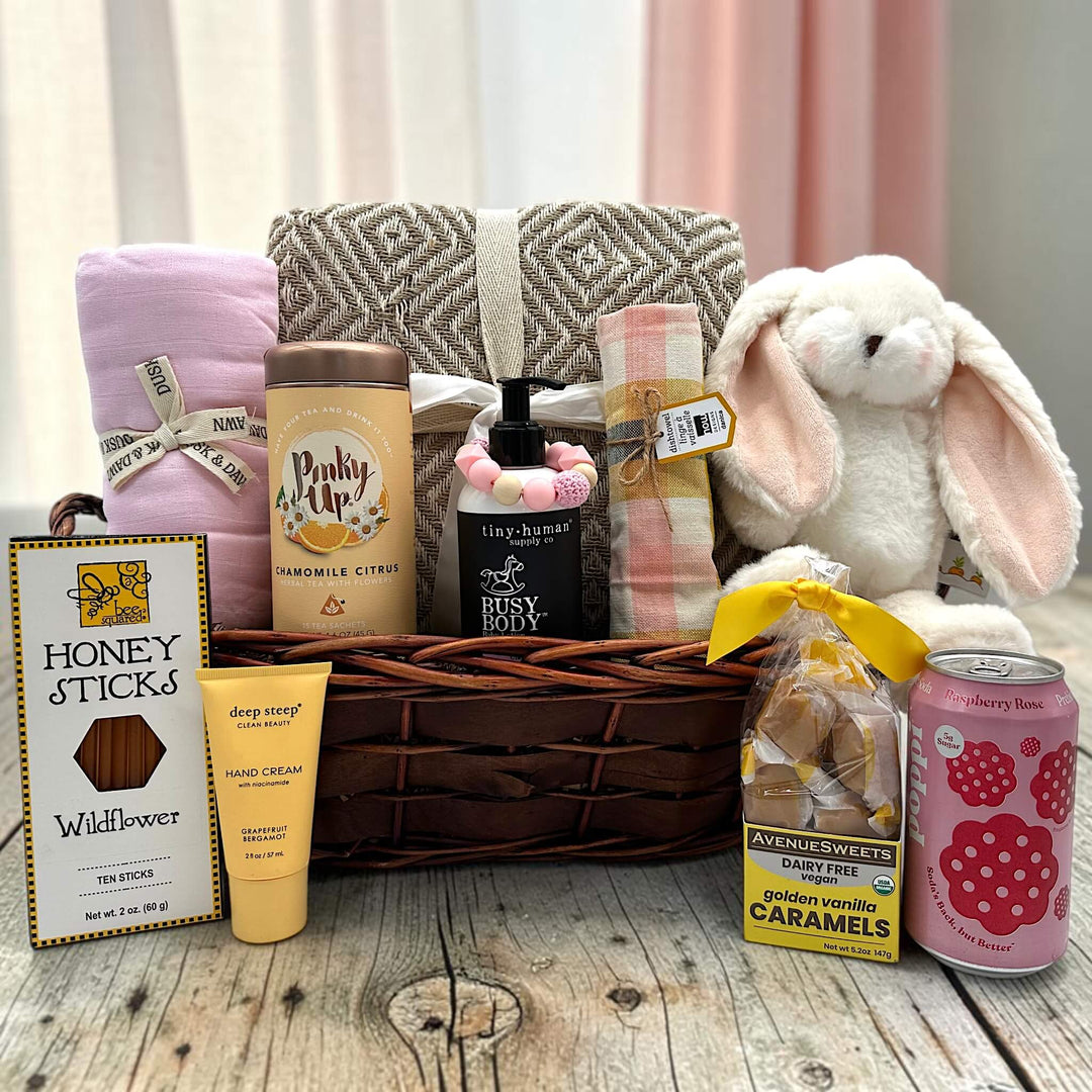 wicker basket with blanket, swaddle, tea, shampoo, teething ring, dishtowel, bunny, honey, lotion, caramels, and poppi