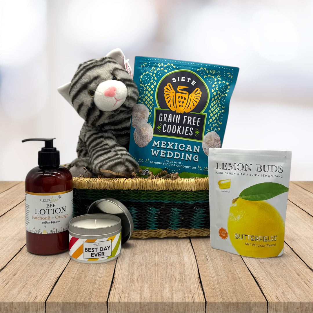 Kitten and cookies sitting on an african market basket with lotion, a best day ever candle and lemon buds sitting on a table
