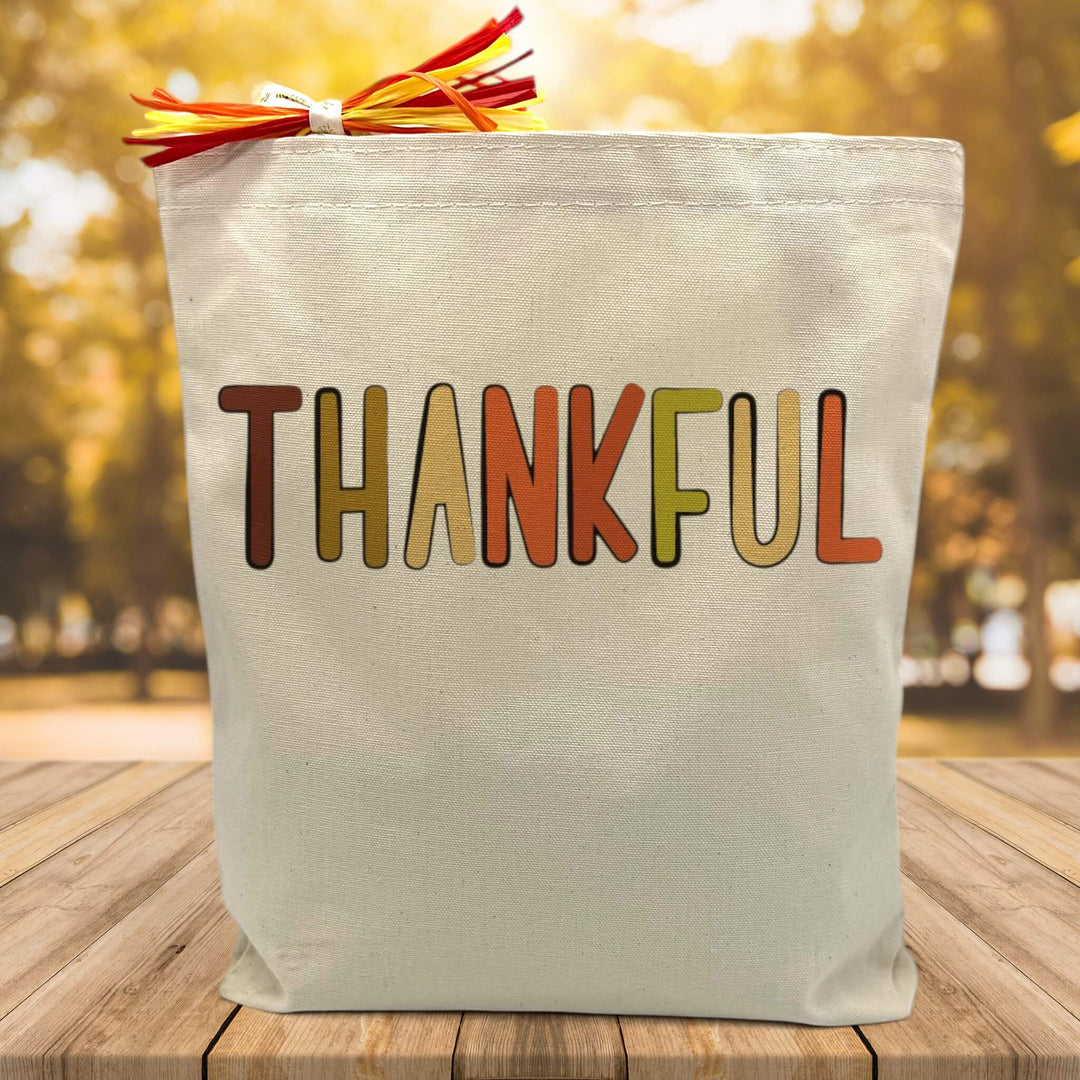 fall colored thankful script printed on a canvas tote bag sitting on a table with a blurred fall background