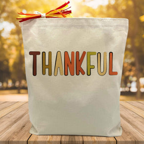 fall colored thankful script printed on a canvas tote bag sitting on a table with a blurred fall background