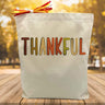 fall colored thankful script printed on a canvas tote bag sitting on a table with a blurred fall background
