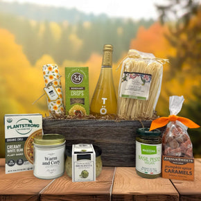 large basket filled with crackers, sparking juice, pasta, chili, a candle, bruschettea, pesto an caramels