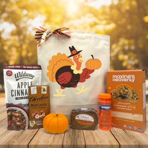 turkey designed gift basket with granola, chocolate, knit pumpkin, bread, bubbles and cookies sitting on a table