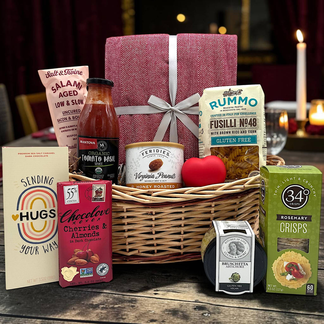 wicker basket with a blanket, salami, pasta and sauce, peanuts, chocolate bars, bruschetta, and crackers