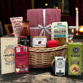 wicker basket with a blanket, salami, pasta and sauce, peanuts, chocolate bars, bruschetta, and crackers
